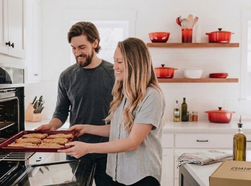Pareja sacando milanesas del horno en su cocina con caja CUATRIS
